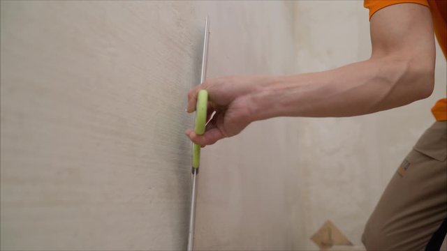 a close shot at the builder hands, who level the wall with a long spatula and plaster, the man applies the composition on the surface. Worker aligns the wall with a spatula. Worker aligns the wall wit