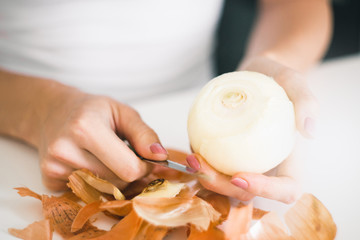 Young woman's hands peel fresh onion head on white background 