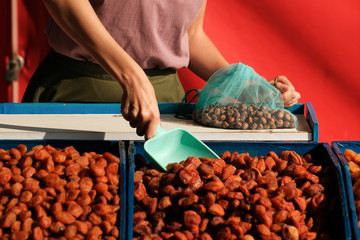 Dried fruit seller. young woman imposes dried apricots and weighs it for the buyer.