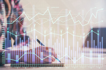 A woman hands writing information about stock market in notepad. Forex chart holograms in front. Concept of research. Double exposure