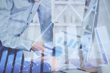 Double exposure of chart with businessman typing on computer in office on background. Concept of hard work.