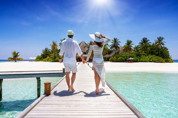 Ein glückliches Paar im Urlaub läuft händehaltend über einen Steg auf eine tropische Insel auf...