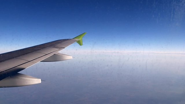 Airplane wing. Airplane flying high in the sky, above clouds, a clear day. Flying in the troposphere, over the planet. Wing with a green engine attached to it. Travel, tourism and vacation concept.