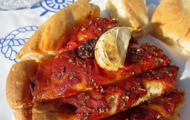Piece of cheeseless pizza cut into strips with tomato sauce, olives, oregano and a clash of garlic.
