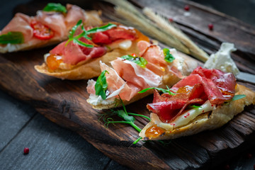 Traditional Bruschetta set with Parma dried ham and prosciutto. Italian antipasti  sandwiches with jamon, cottage cheese, arugula, and sun-dried tomatoes on a rustic wooden Board