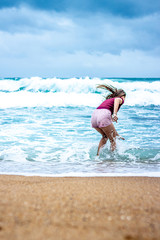 A young teen girl plays in the waves with a storm brewing in the background along the Ballito coastline in South Africa 