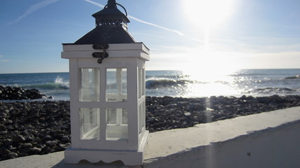 Candlelight flashlight standing on a wall against the background of a pebble beach and a rough sea in the sunlight