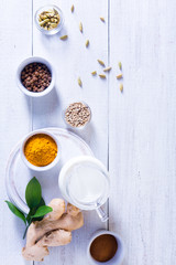 Ingredients for Golden Latte on a white wooden background. Ginger root, milk, turmeric, cardamom, allspice peas.
