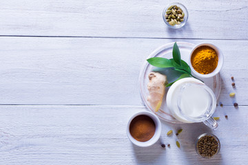 Ingredients for Golden Latte on a white wooden background. Ginger root, milk, turmeric, cardamom, allspice peas.