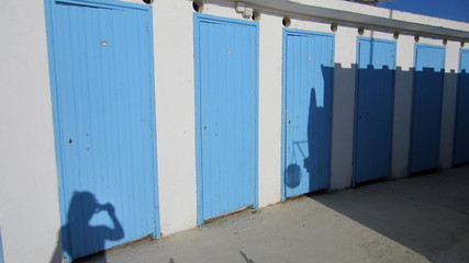 The shadow of the person photographing the blue cabin doors at the seaside on a sunny summer day