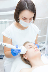 Beautician doctor doing rf-lifting procedure for flawless woman face laying in a beauty salon. Patient receiving electric facial massage. Skin rejuvenation and wrinkle smoothing.