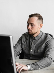 Young businessman or student in a shirt sitting against monitor of computer. Working on a pc at a table in the office with a thoughtful expression. Young businessman working on his laptop in office.