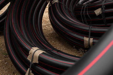 Black rubber or plastic pipes with a red lines as a construction material and equipment at building site. Using as a water pipe.