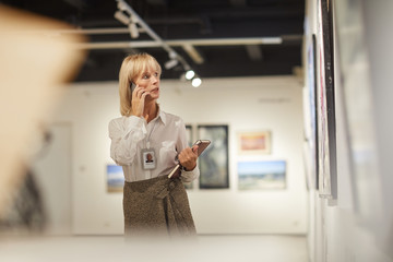 Obraz premium Waist up portrait of female art expert speaking by phone while working at gallery, copy space