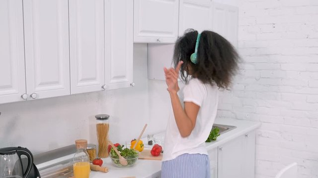 Happy young woman dancing, hacing fun, listening to the music while cooking at the morning. Handheld shot.
