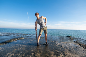 Young fit male training with  athletic rubber on the beach in summer day