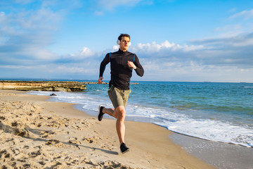 Fit male runner training on the summer beach and listen to music against beautidul sky and sea