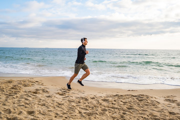 Fit male runner training on the summer beach and listen to music against beautidul sky and sea