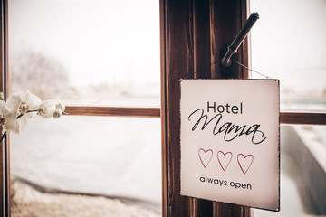 Mama Hotel always open - white square metal plate with text, three hearts hanging on wooden window and white orchid - mother and children dependency concept photograph - vintage effect
