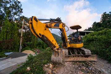 The modern excavator on the construction site with sunset sky. Large tracked excavator standing on a hill with a green grass. Machinery for a construction of a new building in the countryside.