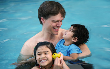 Caucasian father in pool with biracial children, holding disabled son