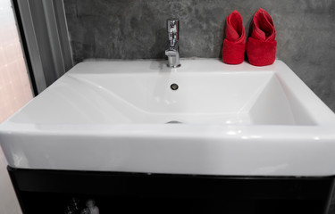 Modern stainless steel faucet with wash basin sink with a two red towels on it . Counter bathroom interior contemporary. Luxury and stylish design bathroom with a concrete style walls.