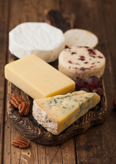Selection of various cheese on the board on wooden table background. Blue Stilton, Red Leicester and Brie Cheese on vintage chopping board. Top view