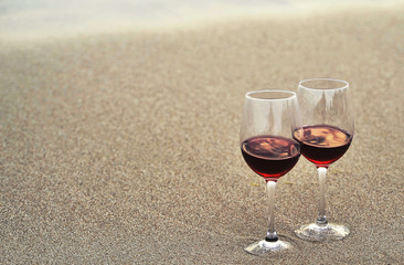 Wine glasses with red wine on sand on the beach. Valentine's Day concept.