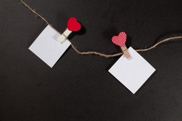 Two paper stickers attached with clothespins on a rope and hand made heart makes. valentines day black background.