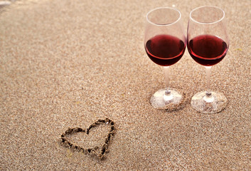 Wine glasses with red wine on sand on the beach. Valentine's Day concept.