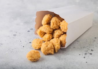 Crunchy southern chicken popcorn bites in white paper container for fast food meals on light background.