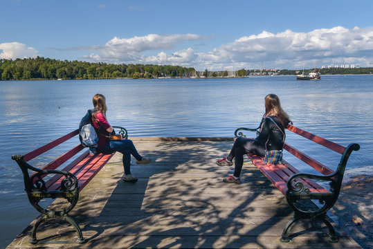 Young women sitting in benches  in the coast of  Djurgarden island of Stockholm city facing to Isbladsviken bay.