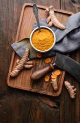 Anti-inflammatory food ingredient, turmeric powder in a ceramic bowl and fresh root on wooden background
