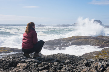 woman looking at the big waves crashing at the rocks of the shoreline on a sunny day on Vancouver Island