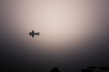 lonely fisherman on a boat in a very strong fog on the lake