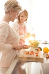 Obraz na płótnie Canvas Smiling mature friends preparing meal in kitchen