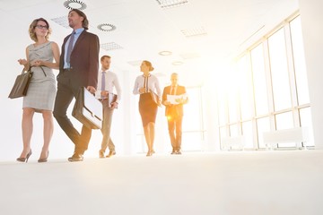 Full length of business colleagues walking while talking in office corridor