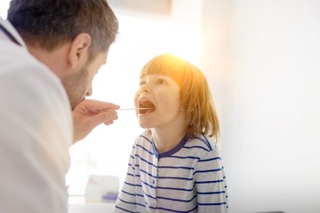 Mid adult pediatrician checking boy patient with depressor at hospital
