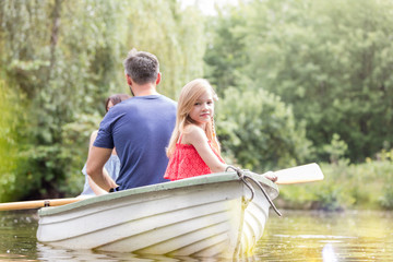 Portrait of cute girl sitting with father on rowboat in lake during summer