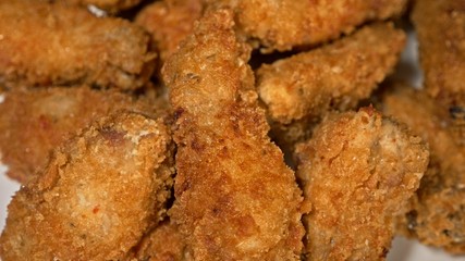Cool beautiful fresh juicy cooked chicken wings in breading. Buffalo wings spread on food white plate in table. Very tasty and beautiful. Cooking with deep fryer fry machine.