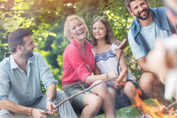 Tilt shot of happy family with male friend roasting sausages over campfire at park