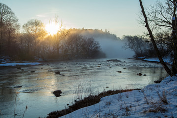 A crispy winter morning with a beautiful sunrise by the river where the fog rises