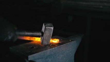 Forge workshop. Smithy manual production. Hands of smith with hammer hit on glowing hot metal, on the anvil, the forging process. Blacksmith makes iron products for manufacture of fireplace, stove.