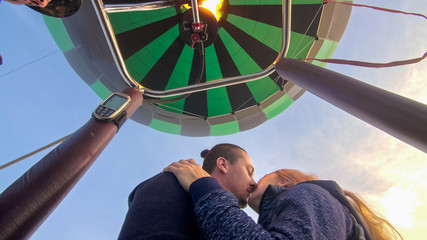 Adventure love couple on hot air balloon watermelon. Man and woman kiss hug love each other. Burner directing flame into envelope. Fly in morning blue sky. Happy people take selfie in hot air ballon.