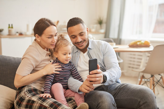 Warm toned portrait of happy mixed-race family taking selfie hoto in home interior, copy space