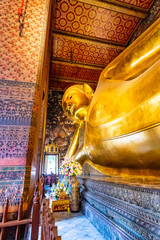 Fototapeta premium Beautiful statue of reclining golden Buddha placed in Wat Pho temple, Bangkok. Spiritual place of buddhism religion with beautiful ornaments on the pillar. Detail view of Buddha's head