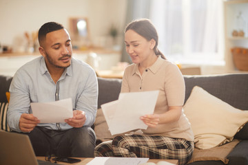 Portrait of adult couple doing paperwork while paying taxes online in cozy home interior, copy space
