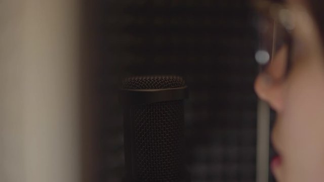 Dolly to reveal female voice actor speaking into a microphone.