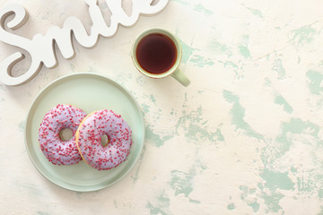 Plate with tasty donuts and cup of tea on light background
