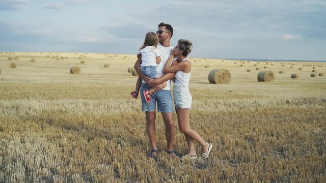 Portrait of young parents with their little daughter have fun among field
